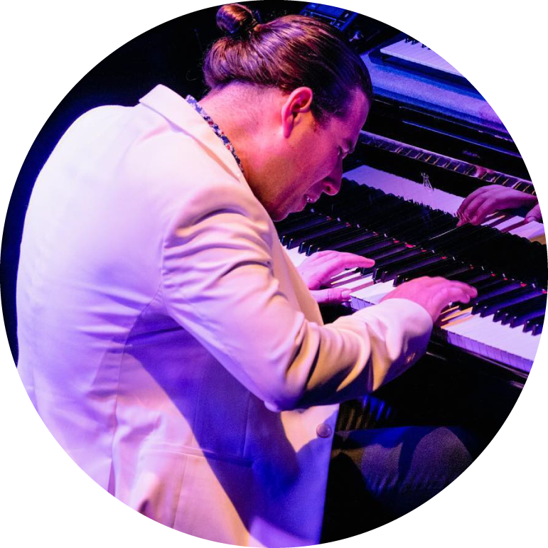 Alfredo Rodríguez wears a white blazer and plays piano live in blue lighting 