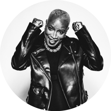 Black & white photo of Angélique Kidjo with her fists up smiling in a leather jacket.