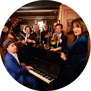 The band poses together around a piano in a room with brown walls