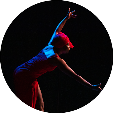 A dancer is captured in motion with red and blue lighting shining down against a black backdrop