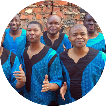 Five members of Ladysmith Black Mambazo pose together smiling in front a brick background.