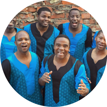 Six members of Ladysmith Black Mambazo pose together with glee in front a brick background.