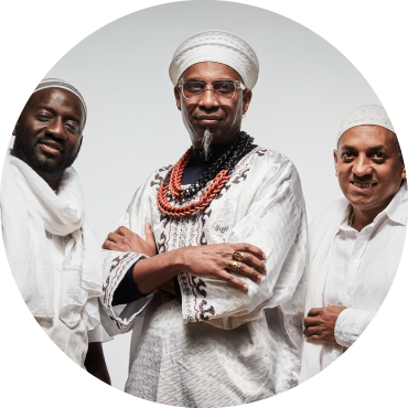 Left to Right: Seckou Keita, Omar Sosa, and Gustavo Ovalles pose together dressed in white against a white background.