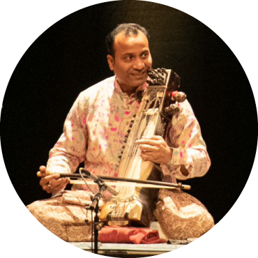 A man plays the sarangi (stringed instrument) and wears traditional Indian clothing.