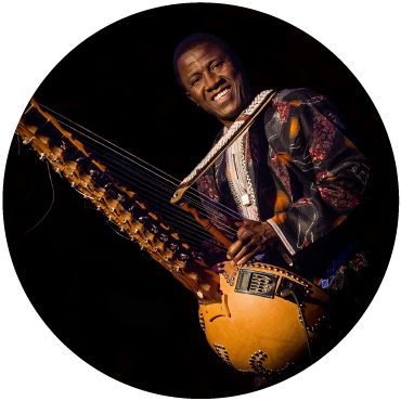 Lamine Cissokho smiles as he plays the kora against a black background.