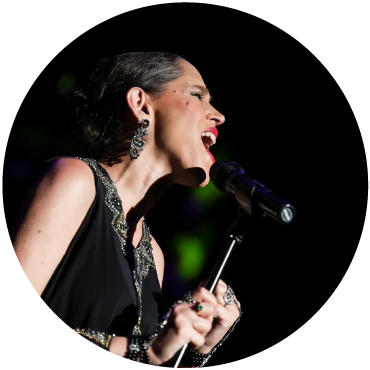 Singer China Forbes passionately sings into a microphone as she wears black against a dark background.