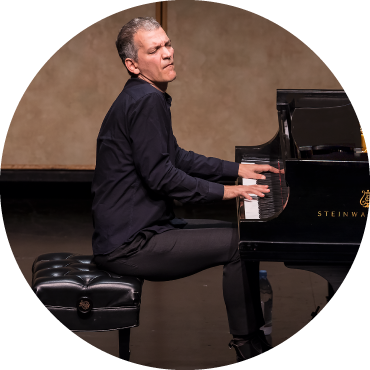 Brad Mehldau wears a black suit and faces to the side as he plays the piano