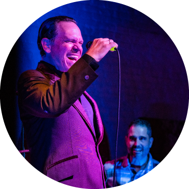 Kurt Elling, dressed in a suit, sings into a microphone with a band member to the right of him 