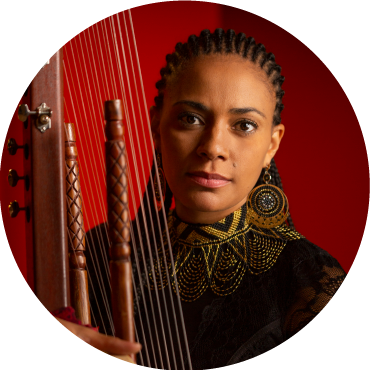 Headshot of Sona Jobarteh posing behind a kora in front of a red background.