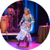 Angélique Kidjo lifts her vibrantly patterned dress as she dances on a stage.