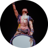 A yamato performer looks up with his arm extended as he holds a drum strapped over his body.