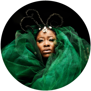 A green veil frames Singer Thandiswa Mazwai face as she stares into the camera against a black background.