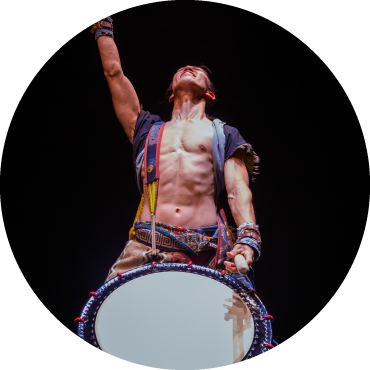 A yamato performer looks up with his arm extended as he holds a drum strapped over his body.