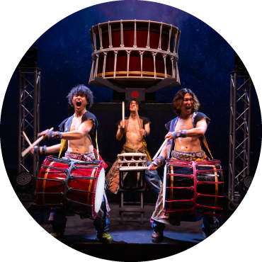 3 yamato performers yell and play huge drums on stage that hang from their bodies.